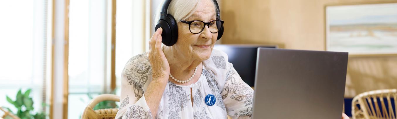 Seniorinainen tietokoneella luurit päässään.